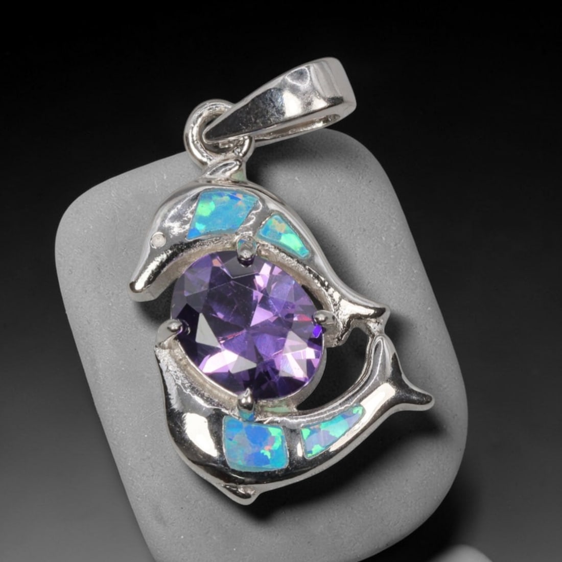 3.69g 925 Sterling Silver Dolphin Pendant - Simulated Opal Amethyst, 23D: Crafted from stamped 925 sterling silver, this pendant features a playful dolphin-shaped openwork design that curves around a central gemstone. Four rectangular segments of simulated opal are inlaid a