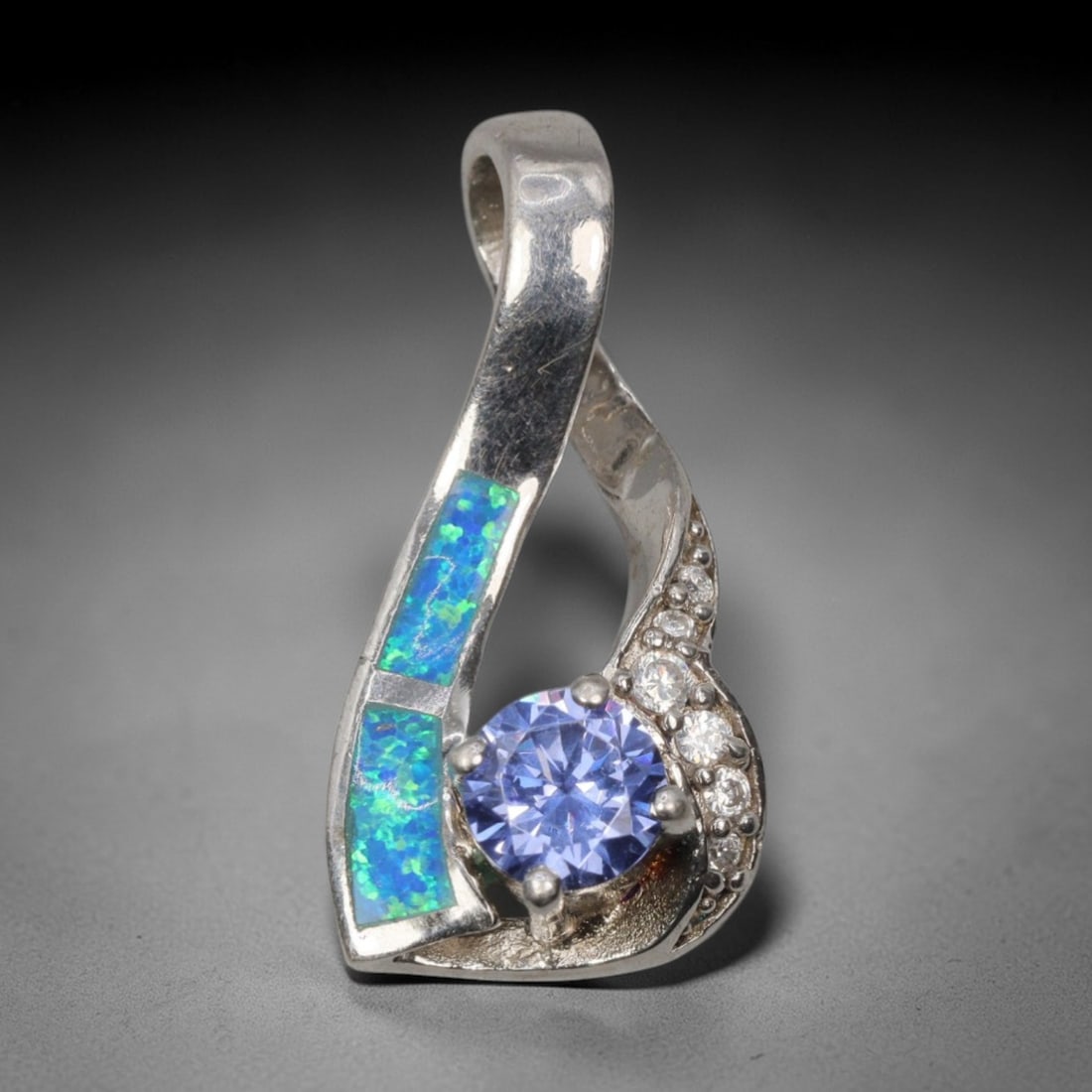 3.96g 925 Sterling Silver Twist Pendant - Simulated Opal Iolite, 26D: Crafted from stamped 925 sterling silver, this pendant features a modern twisted openwork design. Two rectangular segments of simulated opal are inlaid along one curved silver band, exhibiting vivid i
