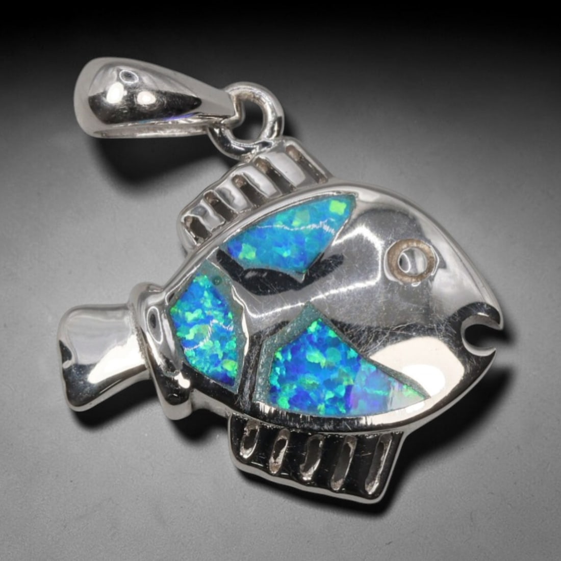 3.49g 925 Sterling Silver Fish Pendant - Simulated Opal, 16D: Crafted from stamped 925 sterling silver, this pendant depicts a stylized tropical fish in polished openwork form. The fish's body is inlaid with three segments of simulated opal, exhibiting vivid iri