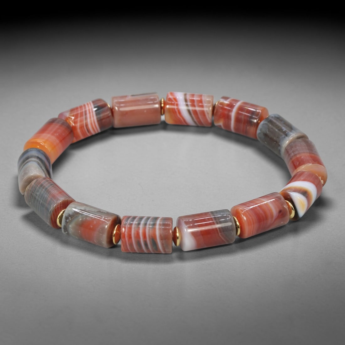 Natural Red Striped Agate Cylinder Beaded Bracelet - Gold-Tone Spacers, 62XV: This bracelet is hand-strung with natural red striped agate cylinder beads, featuring 14 barrel-shaped beads with unique banded patterns in warm red, orange, white, and subtle gray tones. Each agate b