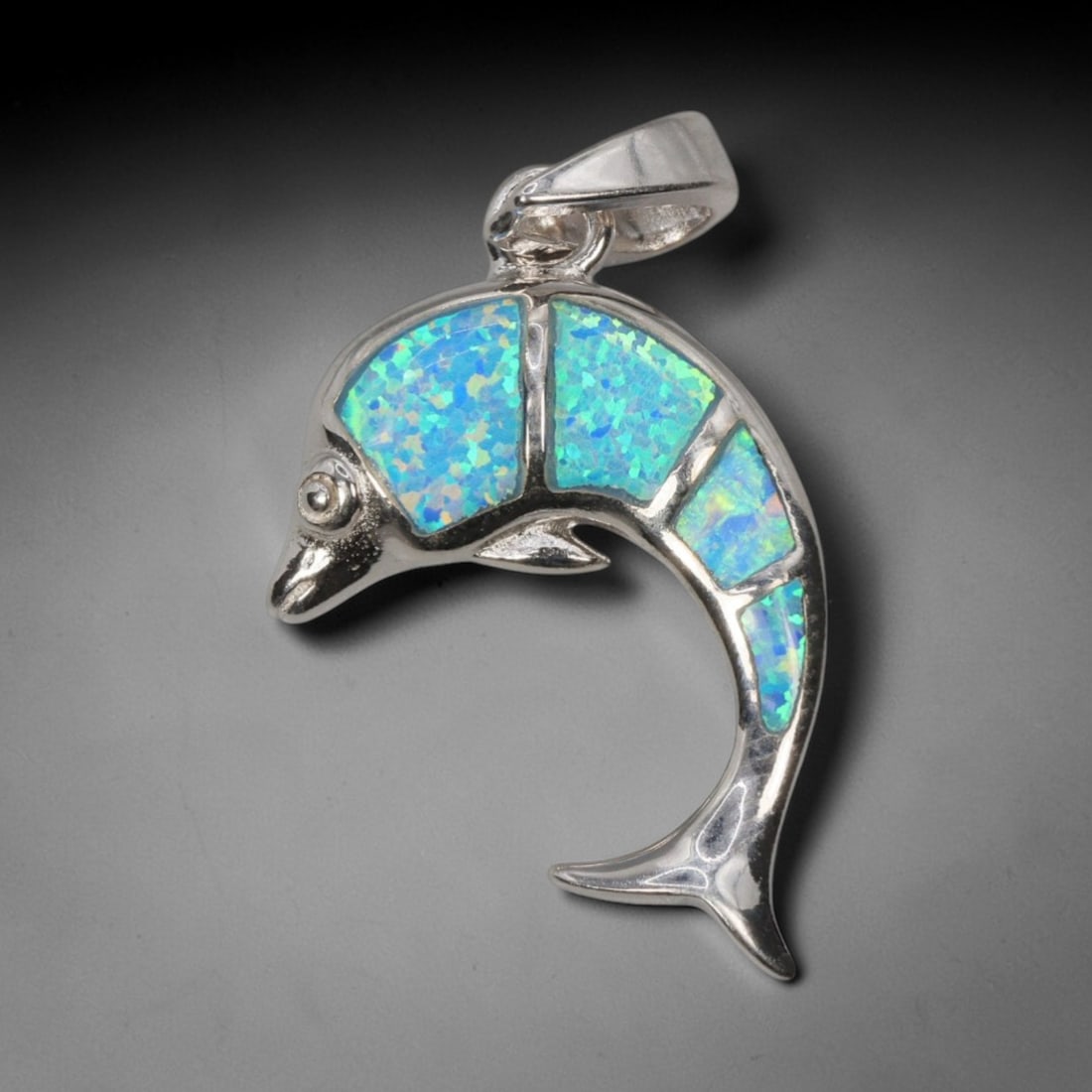 3.74g 925 Sterling Silver Dolphin Pendant - Simulated Opal, 25D: Crafted from stamped 925 sterling silver, this pendant depicts a leaping dolphin in polished openwork form. The dolphin's body is inlaid with four segments of simulated opal, exhibiting vivid iridesce