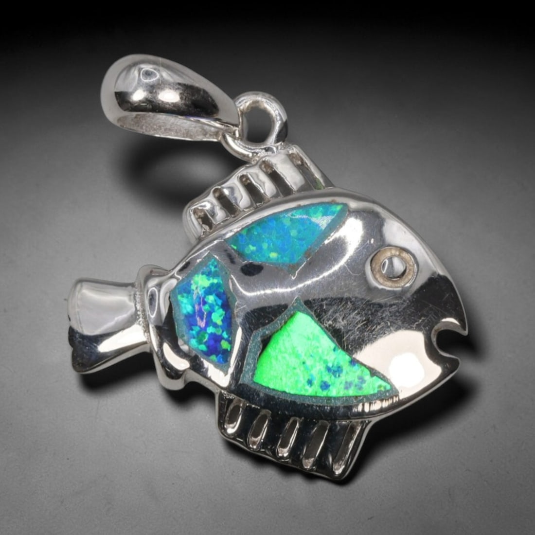 3.27g 925 Sterling Silver Fish Pendant - Simulated Opal, 37D: Crafted from stamped 925 sterling silver, this pendant depicts a stylized tropical fish in polished openwork form. The fish's body is inlaid with three segments of simulated opal, exhibiting vivid iri