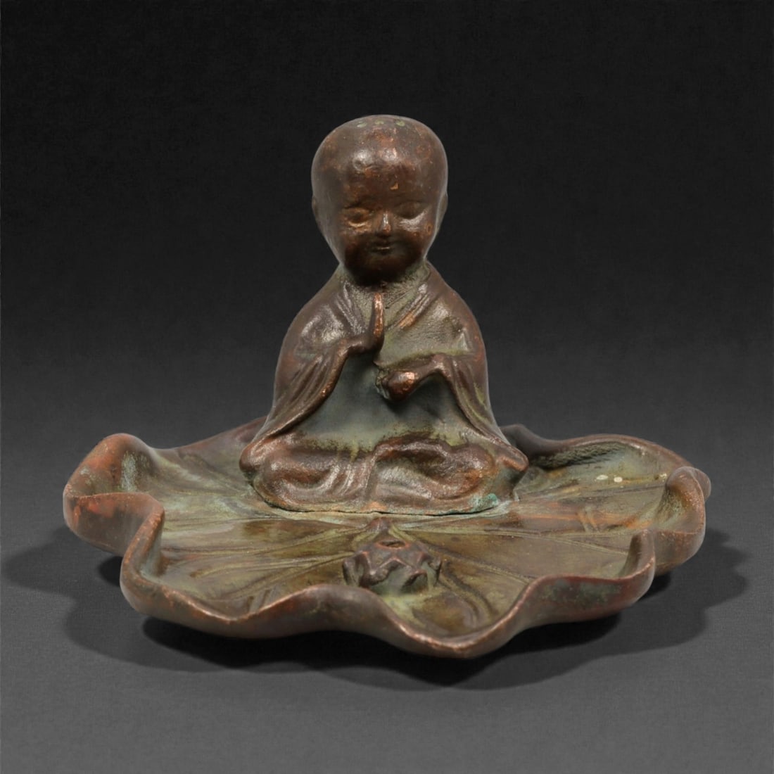 A Chinese Bronze Figure of a Meditating Monk on a Lotus Base, 20th Century, 77YC: Cast in bronze, the figure represents a seated meditating monk shown cross-legged atop a stylized lotus-form base. The figure is modeled with a rounded head, softly defined facial features, and downca