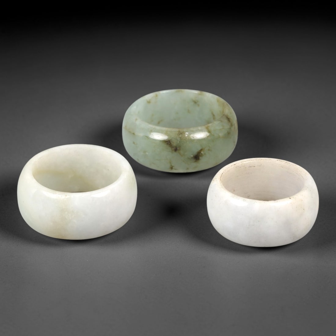 A Trio of Chinese Jadeite Rings - 20th Century, 30AL: Crafted from translucent jadeite in pale celadon and milky white hues, this set of three rings features thick, rounded cylindrical forms with smooth polished surfaces, characteristic of 20th-century C