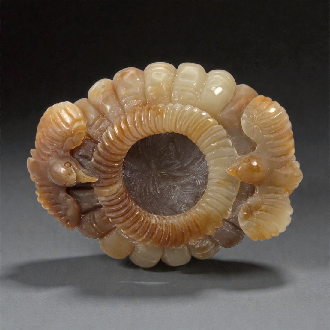 A Chinese Hetian Jade Oval Vessel Plate, Qing Dynasty, 29YB: Carved from pale celadon to honey-toned Hetian nephrite with areas of translucency and darker inclusions, the vessel plate is worked in an oval form with a central circular aperture. The exterior is c