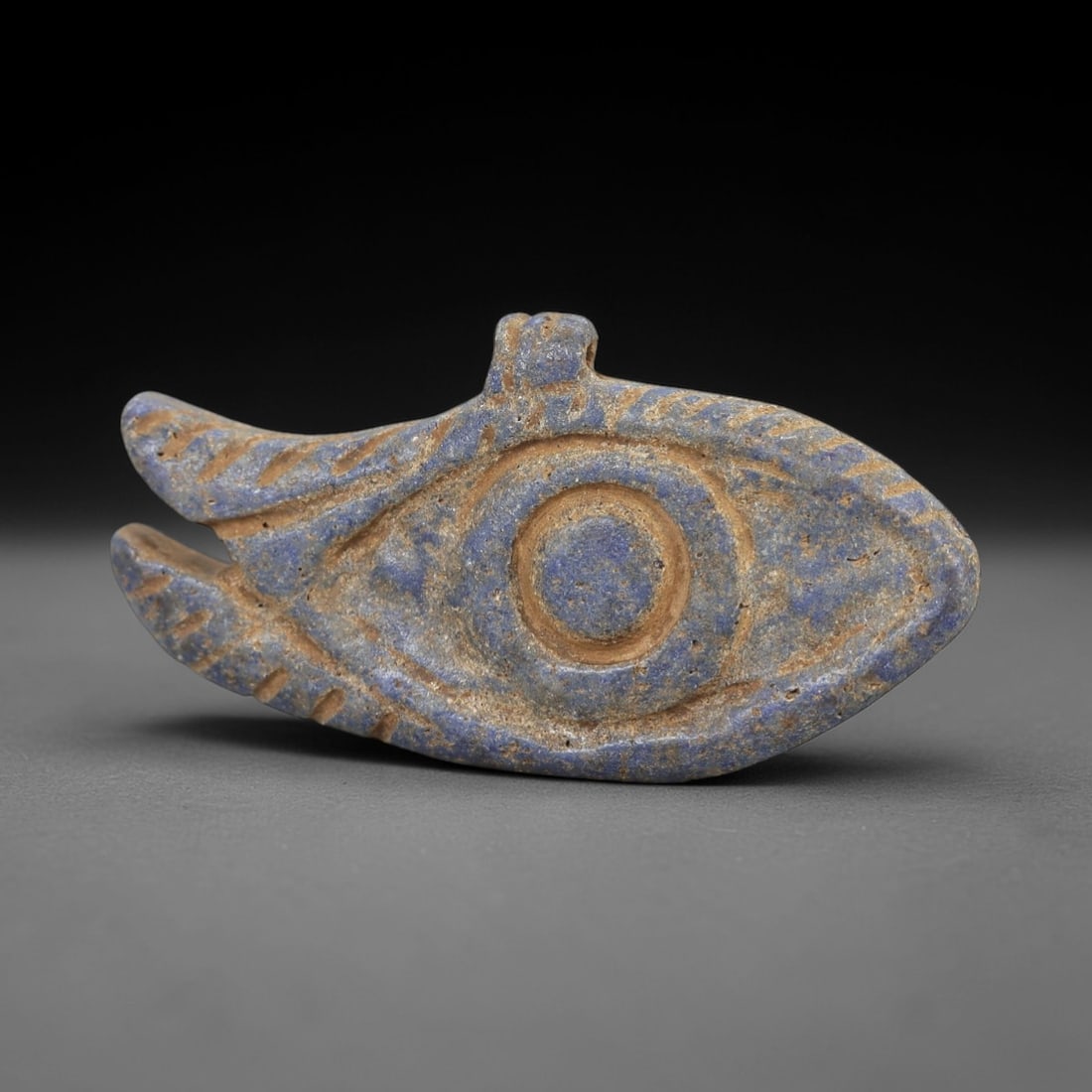 Ancient Lapis Eye Amulet - Egyptian Wedjat Figure, 49AM: This amulet is carved from lapis lazuli, a stone revered in ancient Egyptian culture for its celestial associations and protective symbolism. The form is a classic Wedjat eye, rendered in relief with