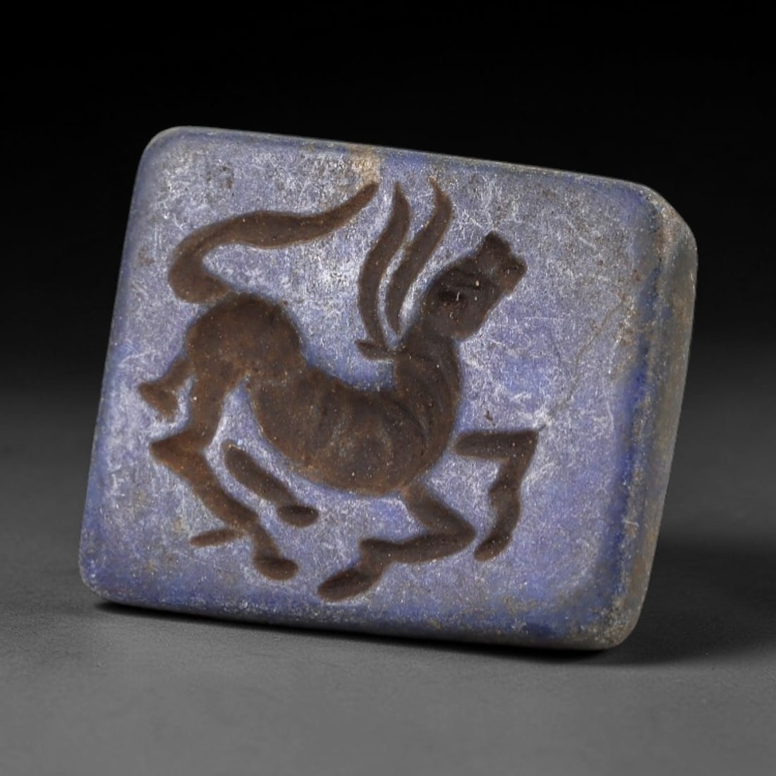 Ancient Lapis Stamp Seal - Near Eastern Ibex Figure, 42AM: This stamp seal is carved from lapis lazuli, a material prized in ancient Near Eastern glyptic traditions for its vivid hue and symbolic resonance. The rectangular bezel bears an incised intaglio depi