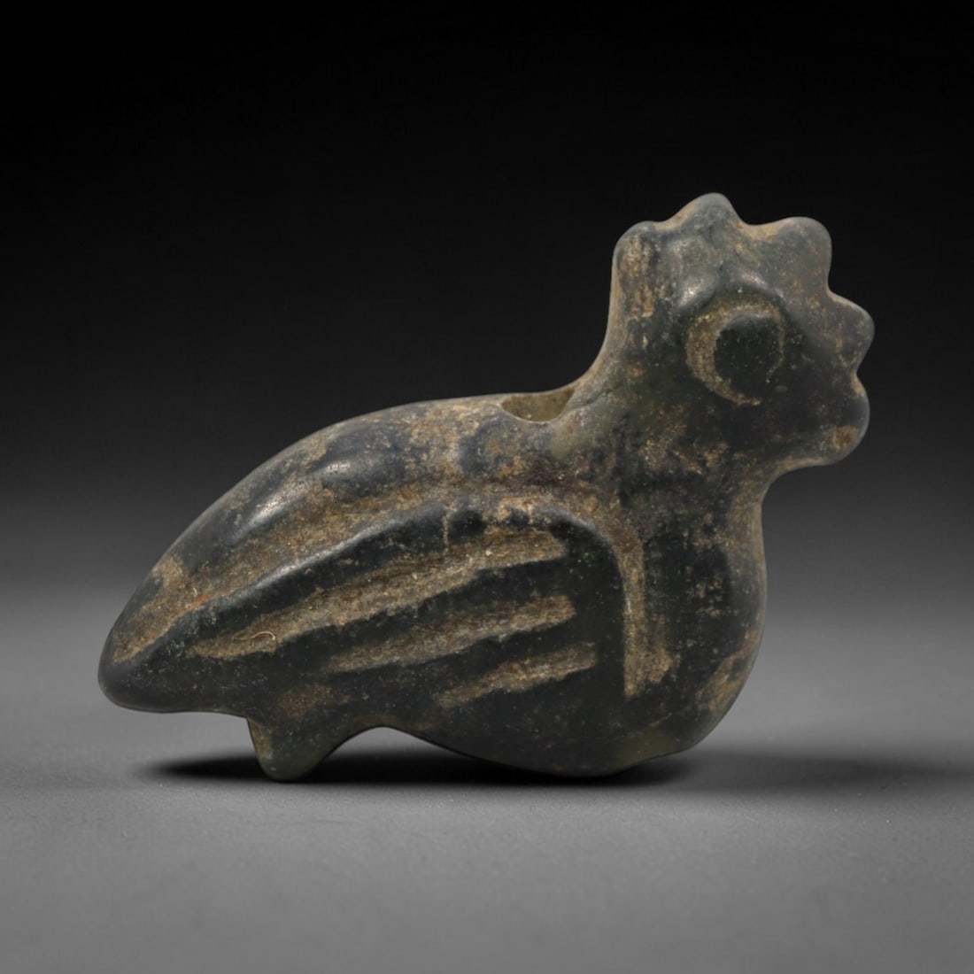 Ancient Near Eastern Stone Bird Amulet - Carved Figurine, 95ZW: This amulet is carved from a dense, dark grey stone, likely basalt or a similar igneous rock, with incised linear details defining its stylized avian form. The piece depicts a compact, plump bird with