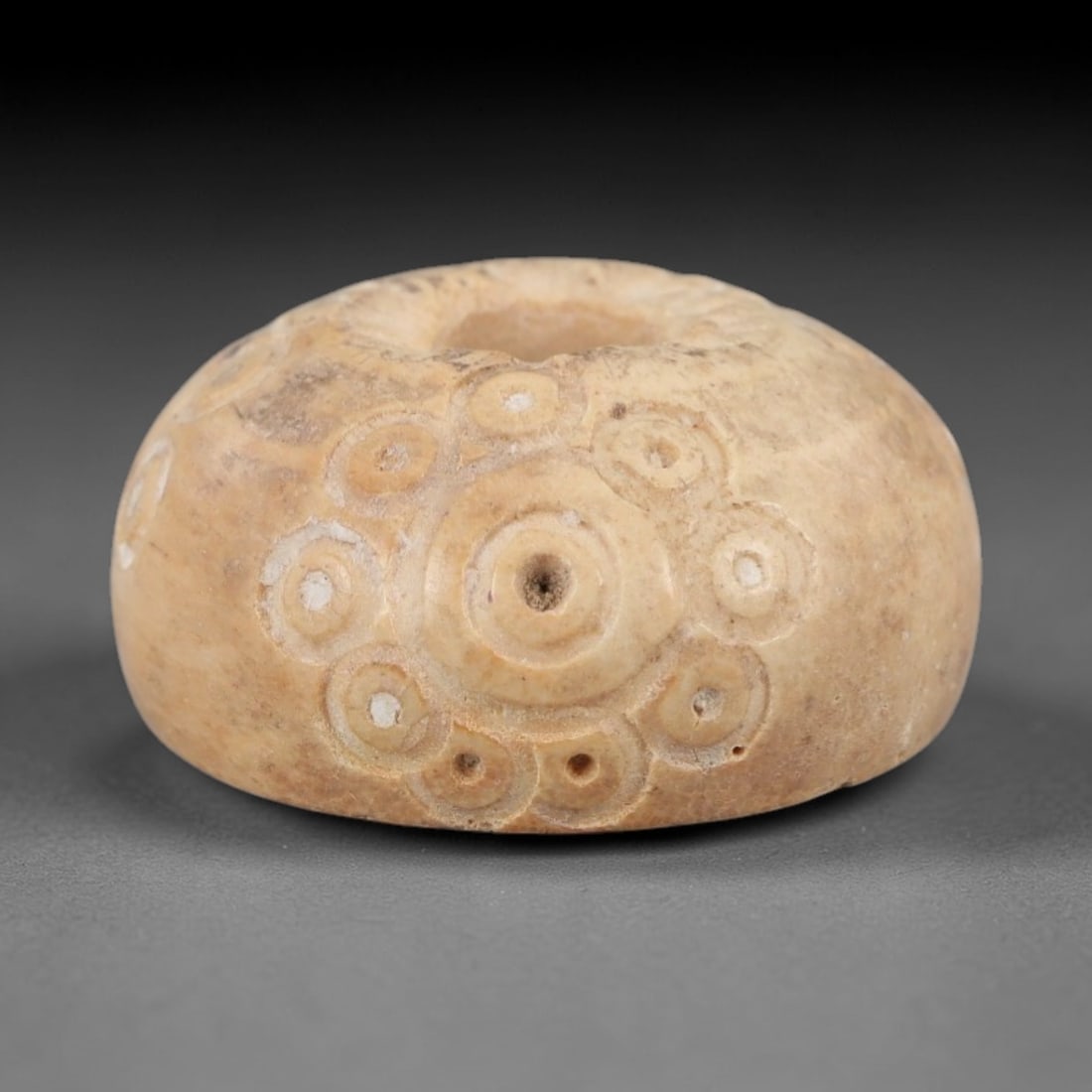 Ancient Bone Spindle Whorl - Near Eastern Dot-in-Circle Motif, 72XR: This ancient Near Eastern spindle whorl is crafted from bone, featuring incised dot-in-circle motifs encircling the central perforation. The compact, rounded form is a traditional textile tool used to