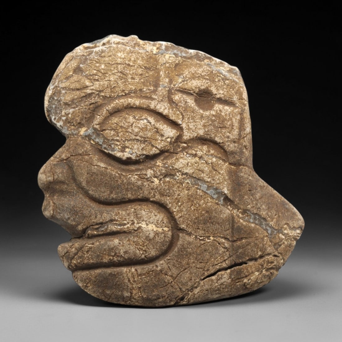 Ancient Stone Anthropomorphic Head - Near Eastern Idol, 85ZV: This artifact is a carved stone anthropomorphic head, rendered in a granular, earth-toned stone consistent with ancient Near Eastern lithic traditions. The relief carving depicts a stylized profile fa