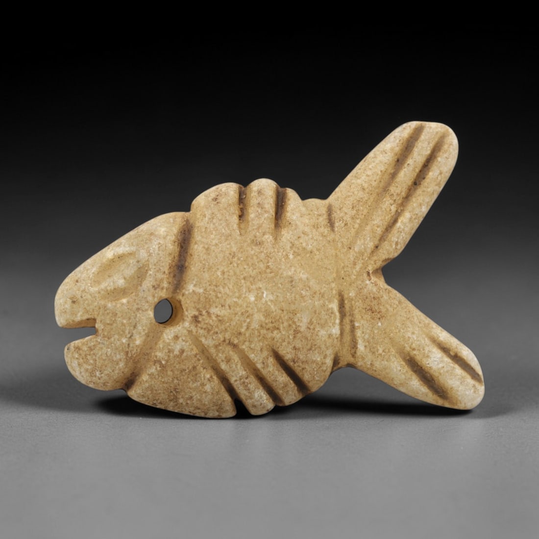Ancient Egyptian Cream Stone Fish Amulet - Carved Pendant Figure, 41ZW: This amulet is carved from a pale cream-colored stone with natural mineral speckling, likely limestone or steatite, featuring a stylized fish form. The piece displays a streamlined body with incised d