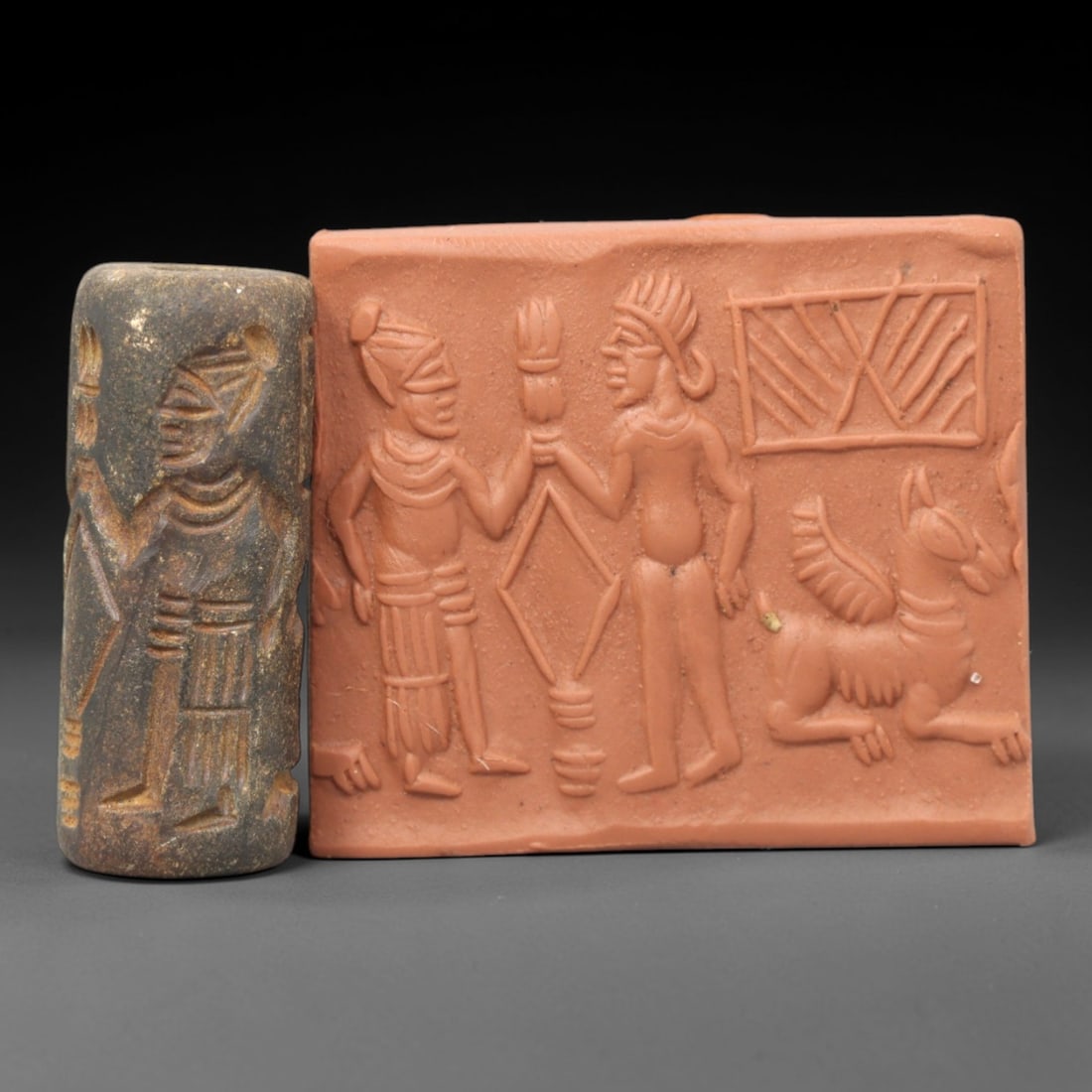 Ancient Steatite Cylinder Seal - Mesopotamian Ritual Exchange & Winged Creature Scene, 3ZP: Carved from dark, weathered steatite, this ancient Mesopotamian cylinder seal depicts a formal ritual exchange scene, executed with precise glyptic craftsmanship characteristic of the Late Bronze or E