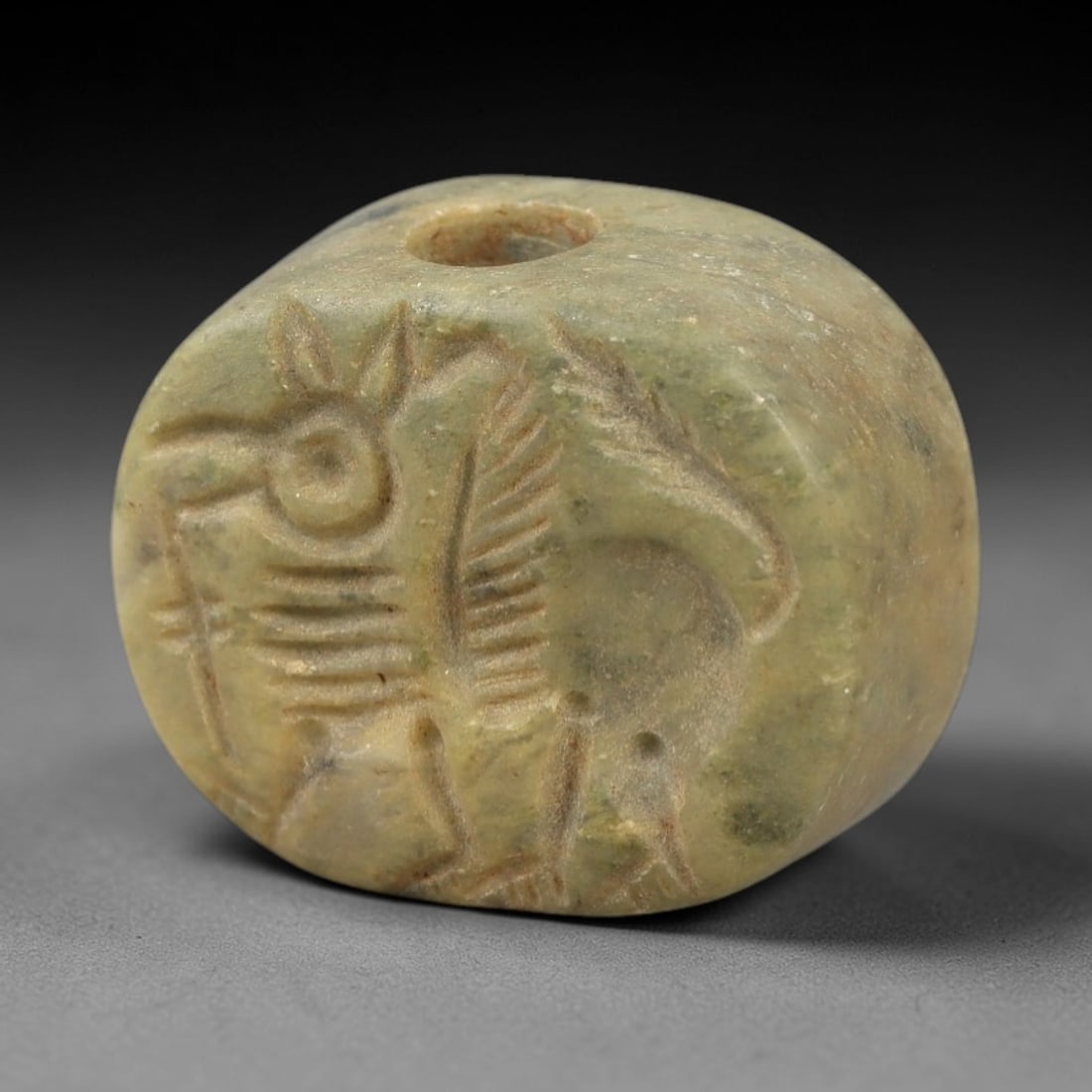 Ancient Steatite Stamp Seal - Near Eastern Mythical Beast Figure, 100AM: Carved from muted green steatite, this hemispherical stamp seal depicts a stylized mythical beast with avian facial features, feathered wings, and quadrupedal limbs, defined by incised linear details.