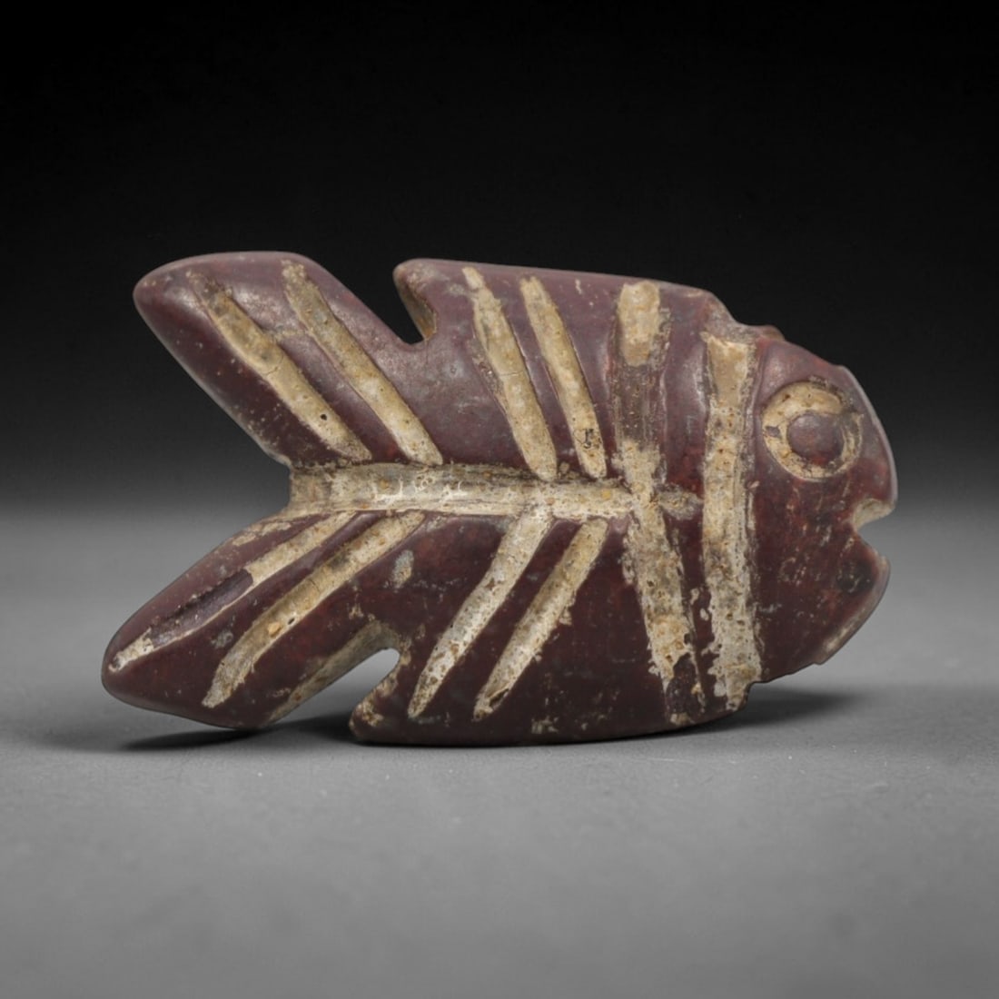 Ancient Egyptian Stone Fish Amulet - Carved Pendant Figure, 55ZV: This amulet is carved from a rich, reddish-brown stone, likely siltstone or a similar sedimentary rock, with deeply incised linear details filled with residual earthy deposits. The piece depicts a sty