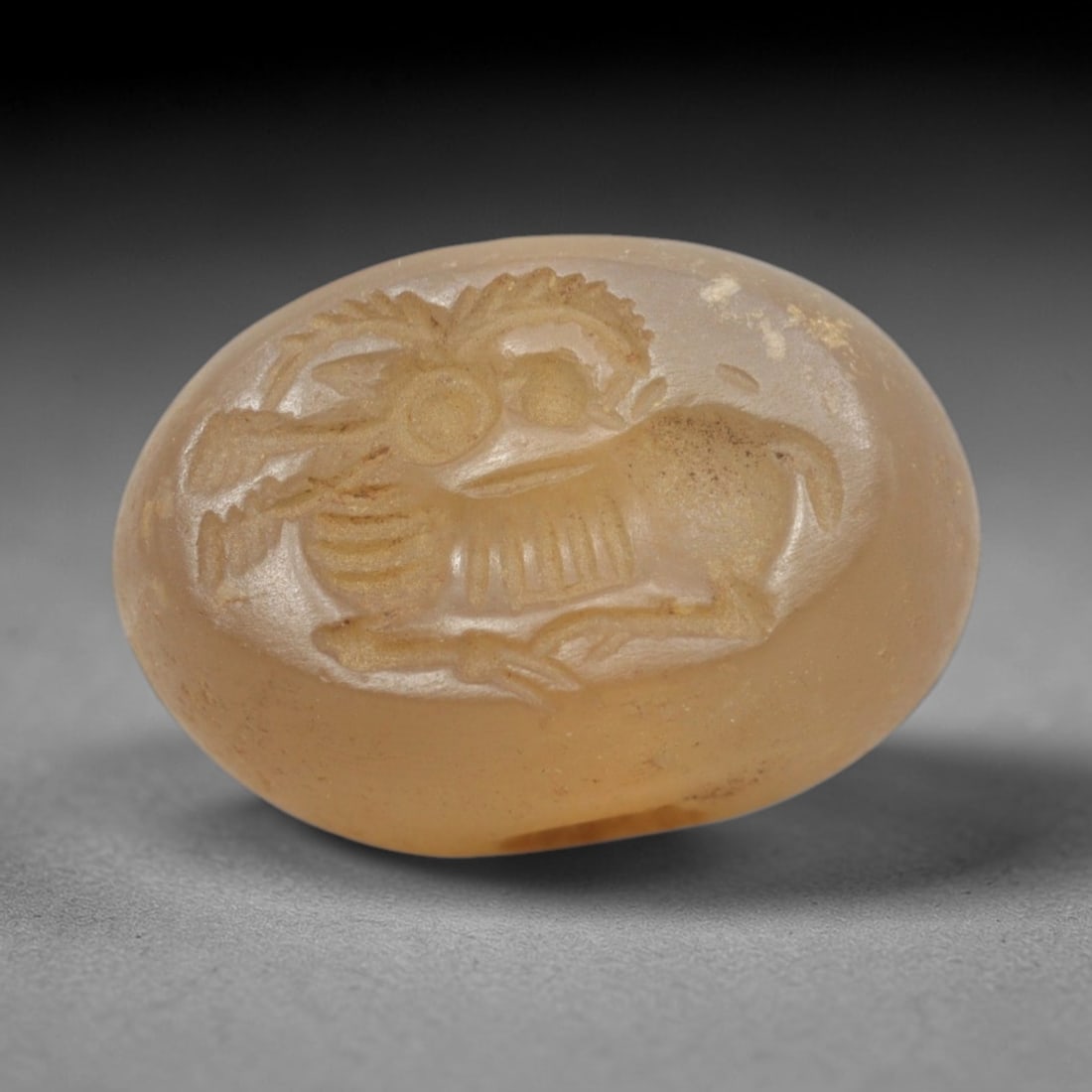 Ancient Chalcedony Stamp Seal - Near Eastern Caprid Figure, 53ZS: Crafted from translucent chalcedony, this oval stamp seal bears a deeply incised profile of a reclining caprid (goat or ibex), rendered with linear detailing to define its curved horns, ribcage, and c