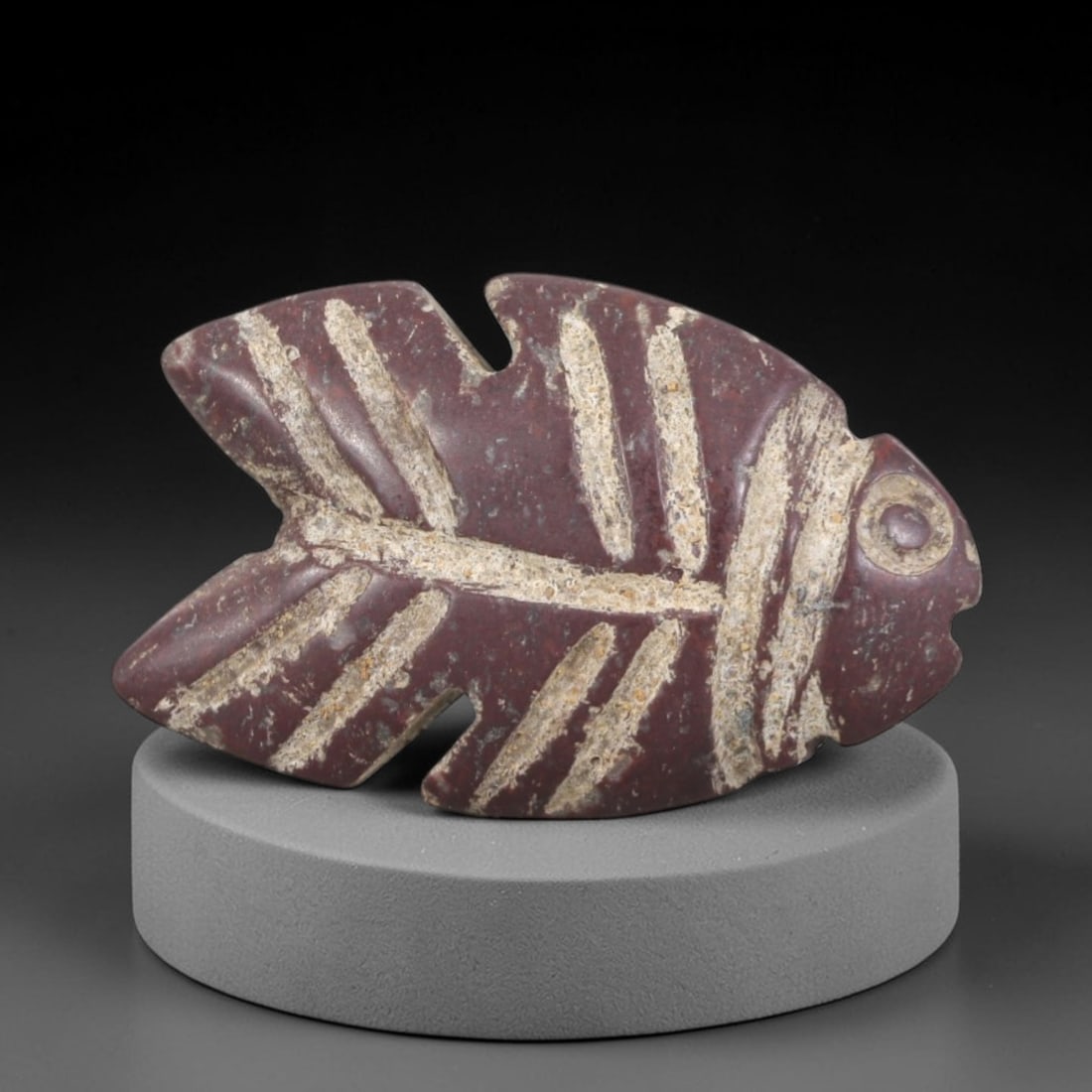 Ancient Stone Fish Amulet - Egyptian Animal Figurine, 46AP: Carved from a dense, reddish-purple stone with natural mineral inclusions and a weathered patina, this amulet depicts a stylized fish form with a rounded head, clearly defined eye, and a body tapering
