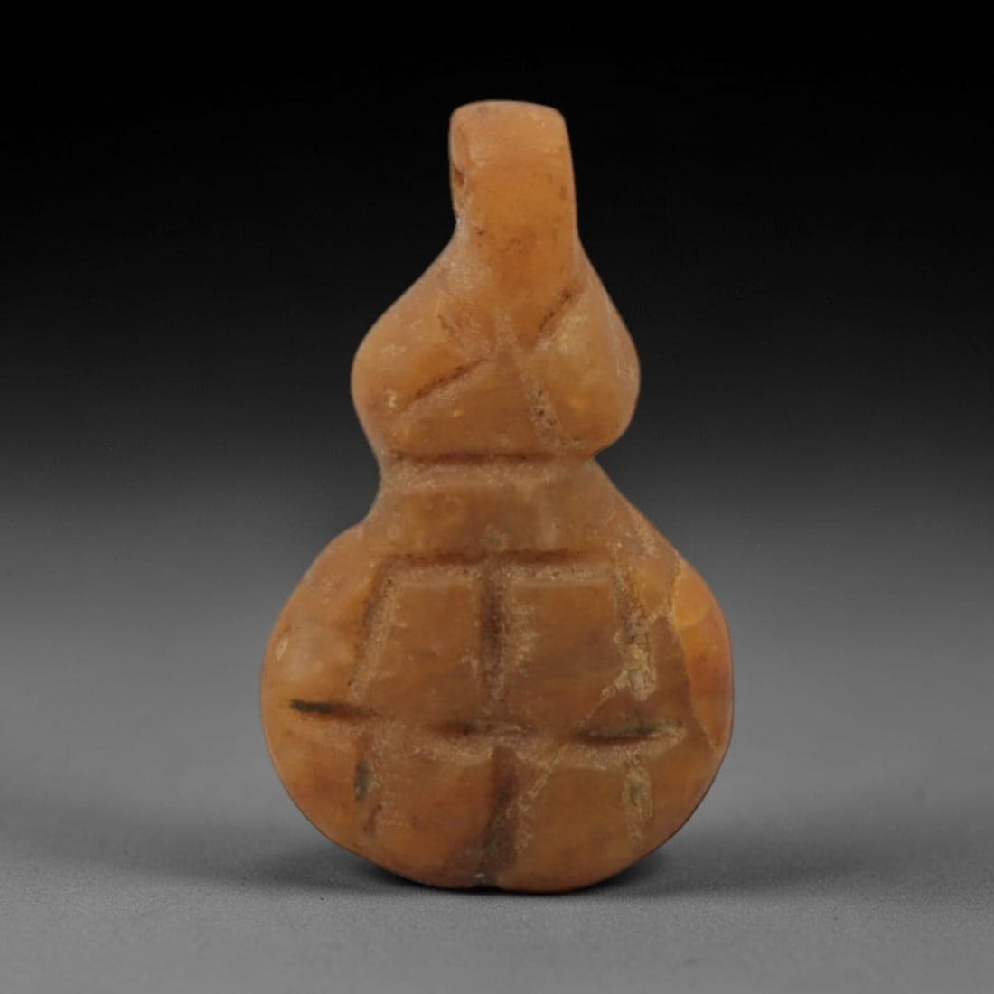 Ancient Stone Gourd - Near Eastern Amulet Pendant, 21XR: Carved from warm orange-brown stone, this amulet is shaped like a stylized gourd with incised geometric patterns and a raised suspension loop at the top. The botanical design is characteristic of Anci