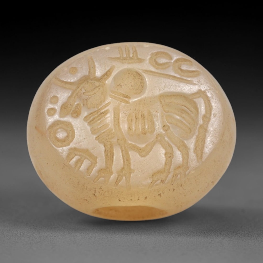 Ancient Chalcedony Hemispherical Stamp Seal - Near Eastern Bull & Script, 42ZP: Crafted from translucent, pale chalcedony, this hemispherical stamp seal bears a deeply incised depiction of a stylized bull, rendered in linear relief with distinct horned head, patterned torso, and