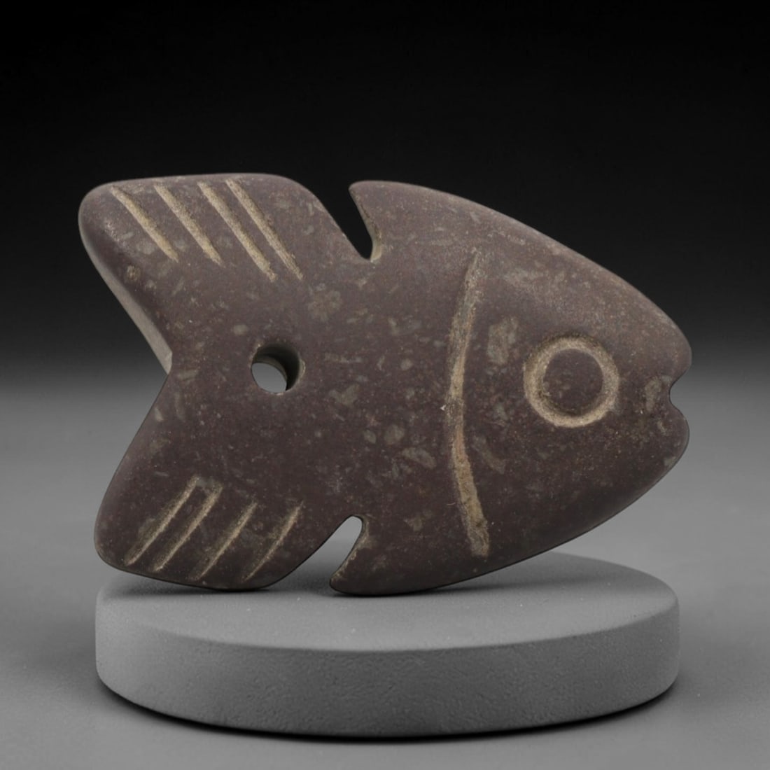 Ancient Egyptian Stone Fish Amulet - Carved Pendant Figure, 61ZV: This amulet is carved from a speckled, reddish-brown siltstone, with incised linear details defining its stylized fish form. The piece features a dorsal fin, ventral fin, a clearly delineated circular