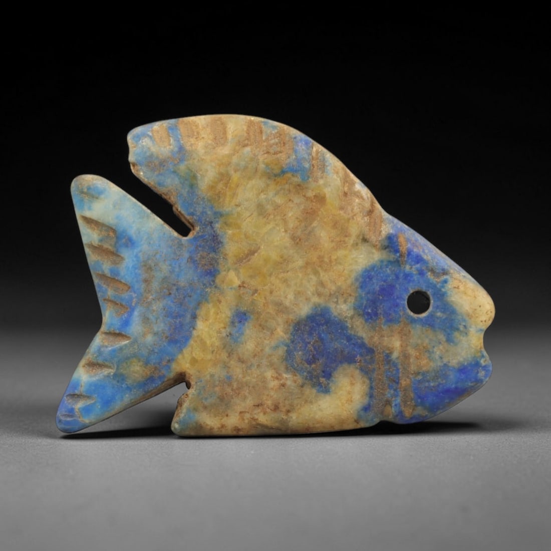 Ancient Lapis Lazuli Fish Amulet - Egyptian Ritual Pendant, 39ZT: Carved from lapis lazuli, this amulet is formed in the shape of a fish, with a pierced hole at the head for suspension, its fins incised with linear details to define the fin rays and segmentation. Th