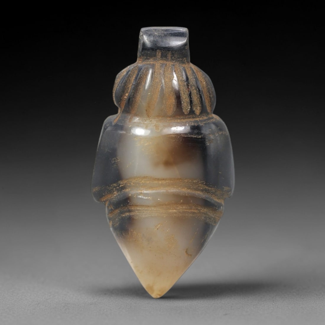 Ancient Agate Amulet - Near Eastern Ritual Pendant, 30XV: Carved from banded agate, this stylized amulet features a tapered, pointed form with incised linear decoration defining a ruffled upper collar and horizontal midsection bands, consistent with ancient