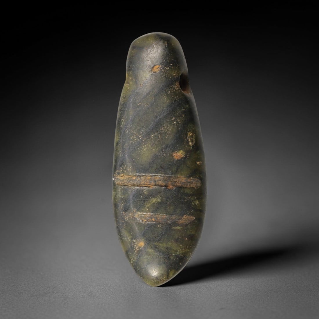 Ancient Green Stone Amulet - Near Eastern Pendant, 58XP: Carved from a mottled green stone, this amulet features an elongated, teardrop form with a single suspension hole at the upper edge, designed for wearable ritual use. Two horizontal incised lines trav