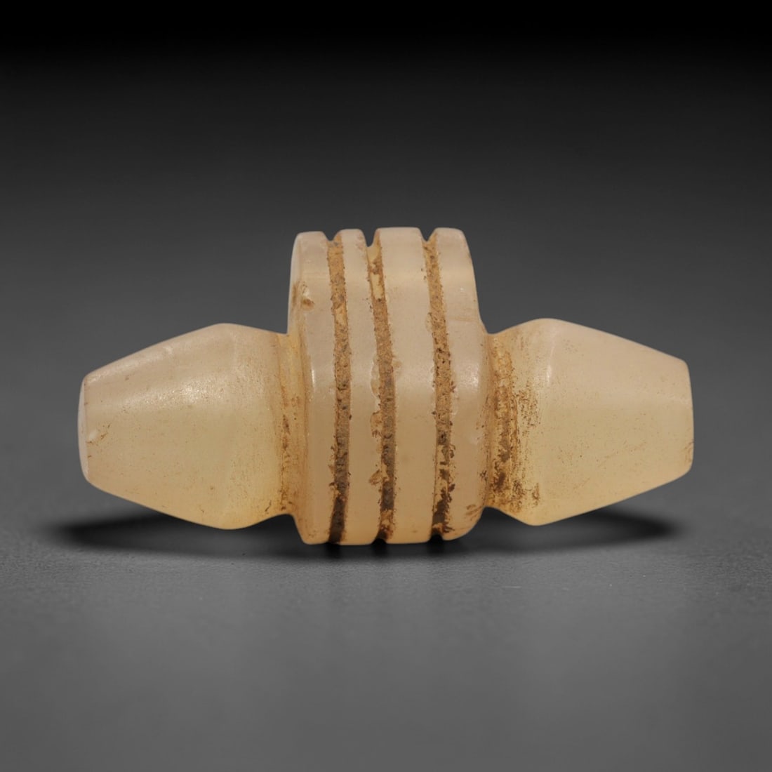 Ancient Achaemenid Chalcedony Amulet - Double-Conical Ritual Object, 68ZR: Carved from translucent pale chalcedony, this double-conical amulet features a central cylindrical segment encircled by four deep horizontal incised grooves, flanked by symmetric tapering ends. The fo