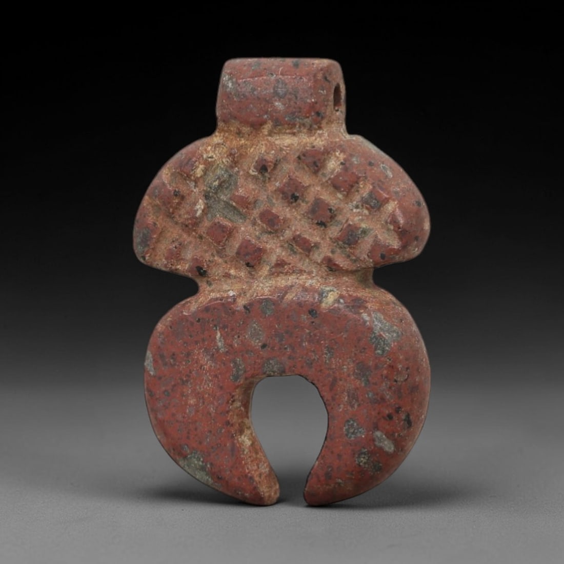 Ancient Stone Anthropomorphic Amulet - Near Eastern Pendant, 77AG: This amulet is carved from a speckled red stone with a weathered, earthy patina. The form is anthropomorphic, with a cylindrical upper segment, a broad torso decorated with incised diamond patterns, a