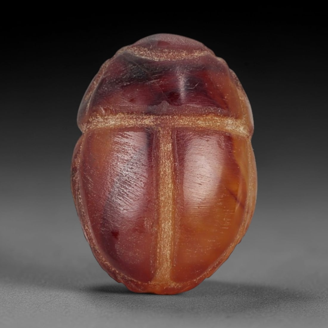 Ancient Banded Carnelian Scarab Amulet - Egyptian Figurine, 28AJ: Carved from rich banded carnelian with deep red to amber gradients, this amulet is formed as a stylized scarab beetle with incised linear detailing to define segmented wing cases and body patterns, co