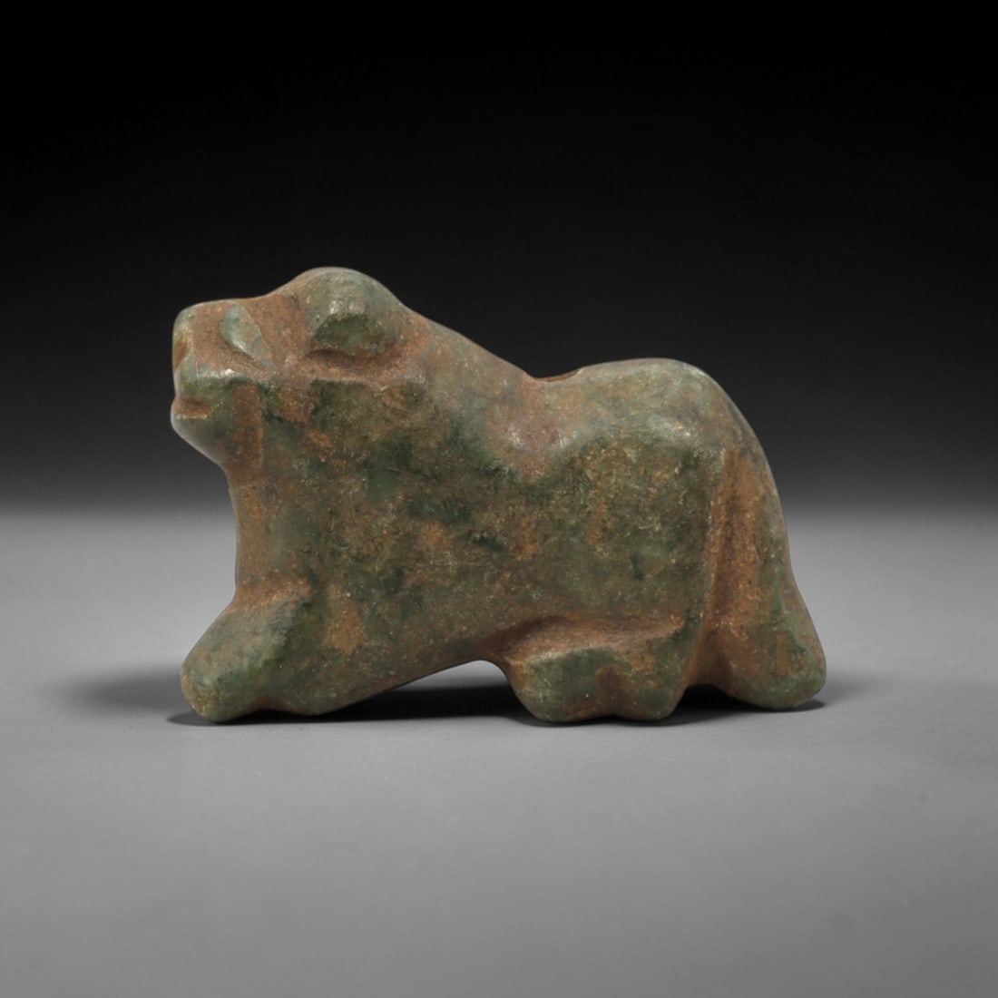 Ancient Serpentine Feline Amulet - Near Eastern Figurine, 96XV: This amulet is carved from mottled green serpentine with natural earthy patina and subtle tonal variations across its surface, executed in a stylized, recumbent form that emphasizes the feline's preda