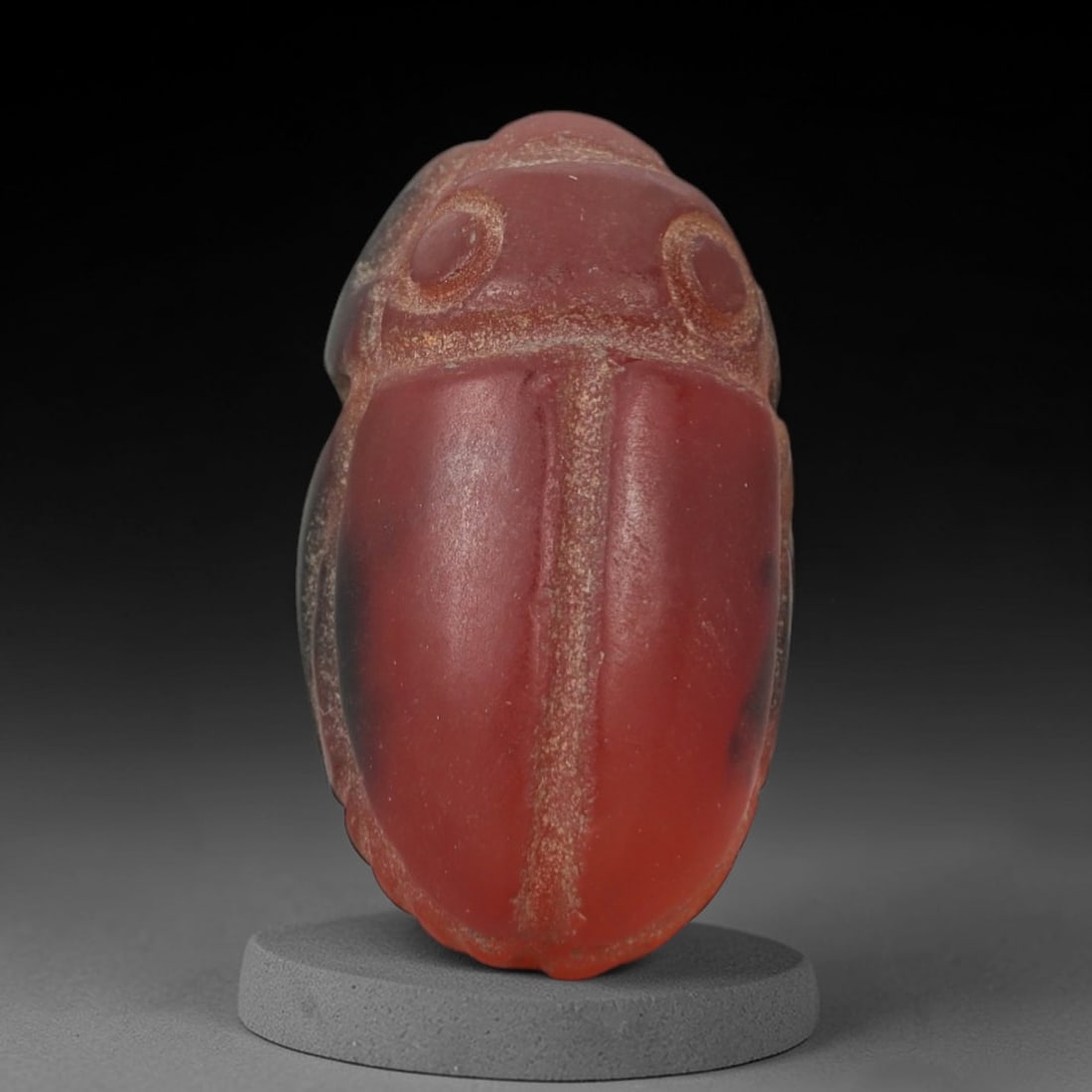 Ancient Carnelian Scarab Amulet - Egyptian Figurine, 80AJ: Carved from rich, deep red carnelian with subtle dark inclusions, this amulet is formed as a stylized scarab beetle with incised linear detailing to define circular eye motifs, central body ridge, and