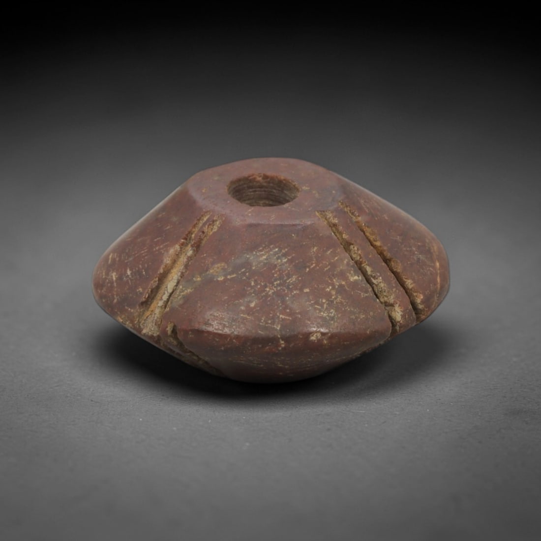 Ancient Red Stone Spindle-Whorl Pendant - Near Eastern Ritual Amulet, 98XP: Carved from a rich, earthy red stone with natural mineral inclusions, this miniature pendant is a stylized spindle-whorl form, a distinctive geometric motif in ancient Near Eastern portable art. The f