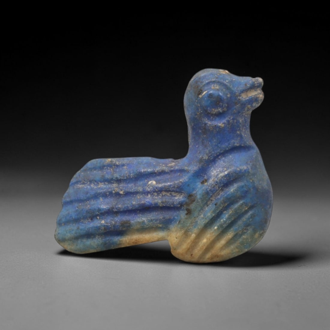 Ancient Lapis Lazuli Bird - Near Eastern Amulet Figurine, 93XV: Carved from lapis lazuli, this amulet depicts a stylized bird with a rounded head, incised eye detailing, and a defined beak. The body is compact, with layered, ridged carvings to represent the wings
