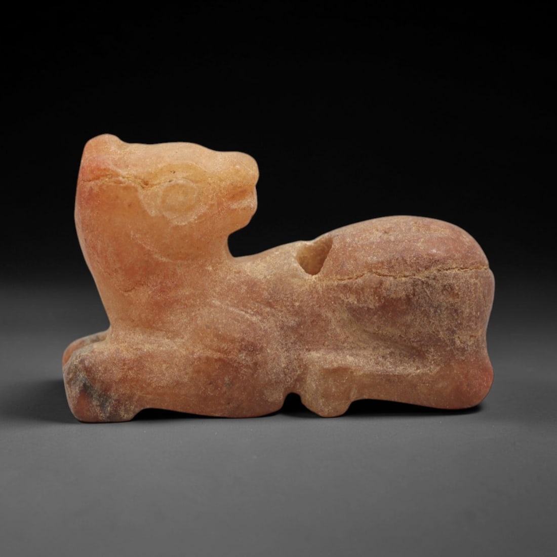 Ancient Carnelian Feline Amulet - Egyptian Figurine, 85XS: This amulet is carved from warm orange-red carnelian, depicting a recumbent feline figure in a crouched, resting posture with incised circular eyes and subtle facial detailing. A pierced suspension ho