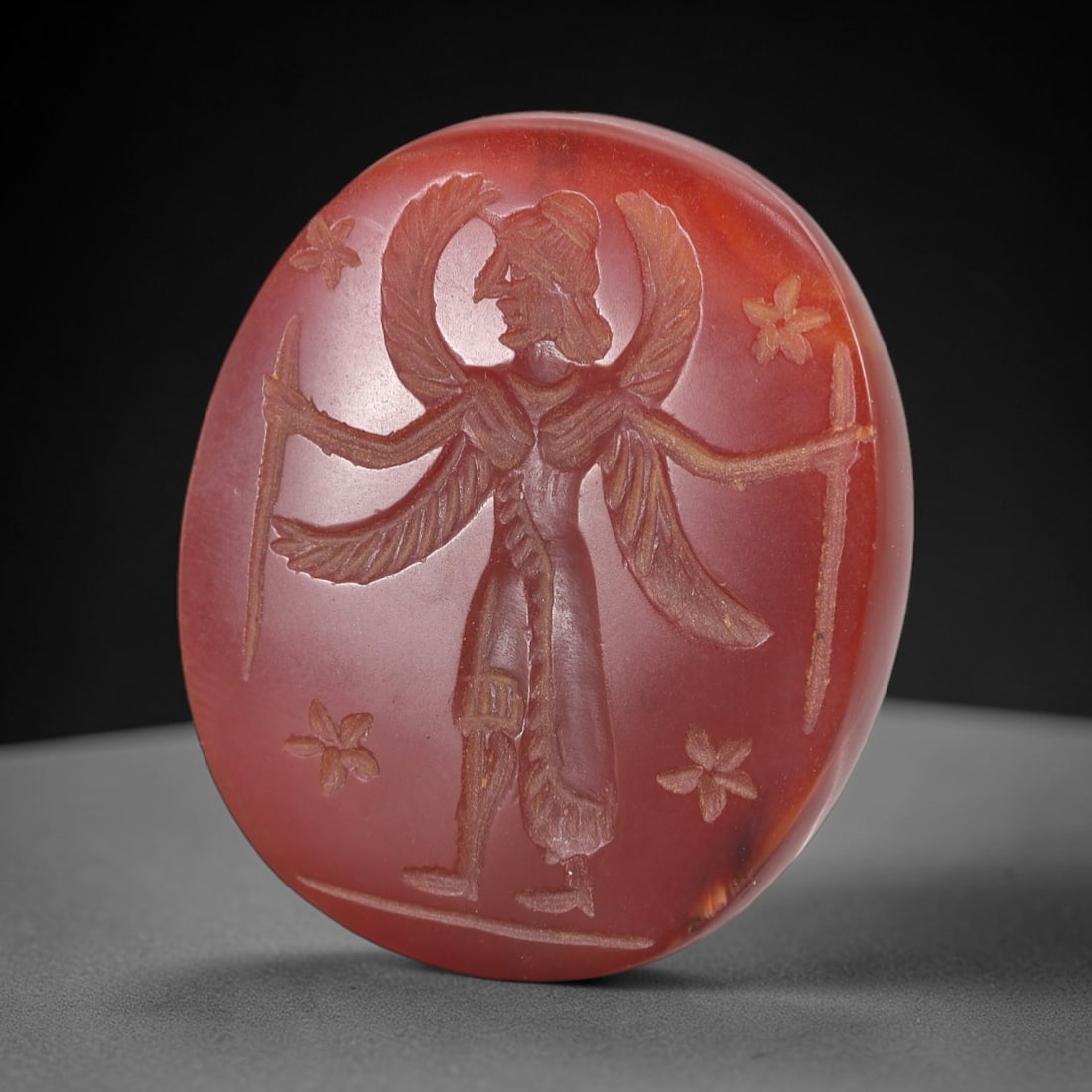 Ancient Carnelian Intaglio Bead - Zoroastrian Genius Figure, 44AM: This substantial oval intaglio bead is carved from rich, translucent carnelian displaying a deep reddish-orange hue with subtle banding and natural crystalline inclusions. The intaglio surface depicts