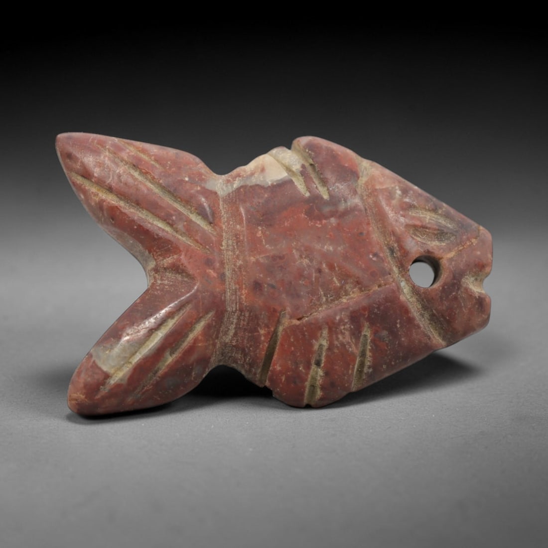 Ancient Egyptian Red Stone Fish Amulet - Carved Pendant Figure, 54ZV: This amulet is carved from a rich, reddish-brown stone with natural lighter veining, likely brecciated jasper or red steatite, with incised linear details defining its stylized fish form. The piece fe