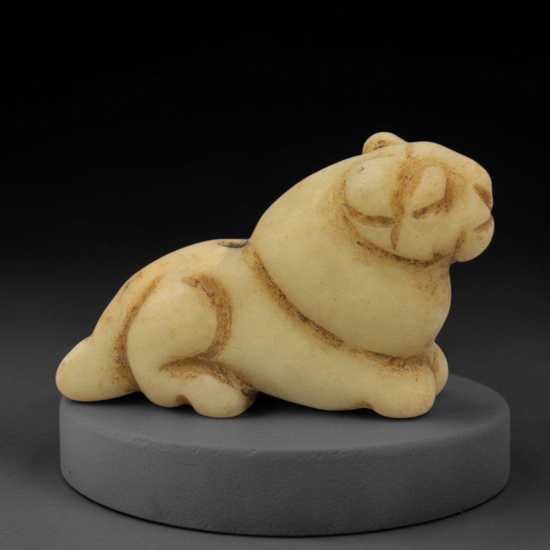 Ancient Stone Recumbent Feline - Egyptian Amulet Figurine, 92XQ: Carved from an off-white stone with warm ochre inclusions, this amulet depicts a recumbent feline, likely a lion or cat, with stylized facial features and a compact, rounded body. The creature rests i