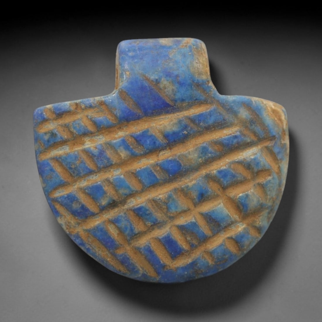 Ancient Lapis Lazuli Amulet - Egyptian Grid Pattern Pendant, 37ZT: Carved from lapis lazuli, this amulet features a semicircular form with a raised rectangular upper lug pierced for suspension, its flat surface incised with a dense grid pattern of intersecting diagon