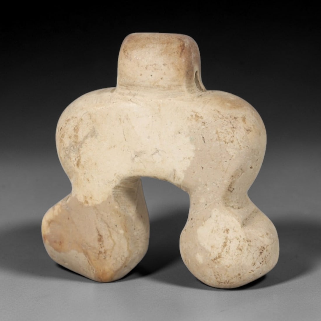 Ancient Stone Amulet - Near Eastern Carved Pendant, 45AR: This artifact is carved from a pale, creamy stone with subtle surface discoloration and mineral variations consistent with age. The form is a symmetrical, abstract pendant with a central cylindrical t