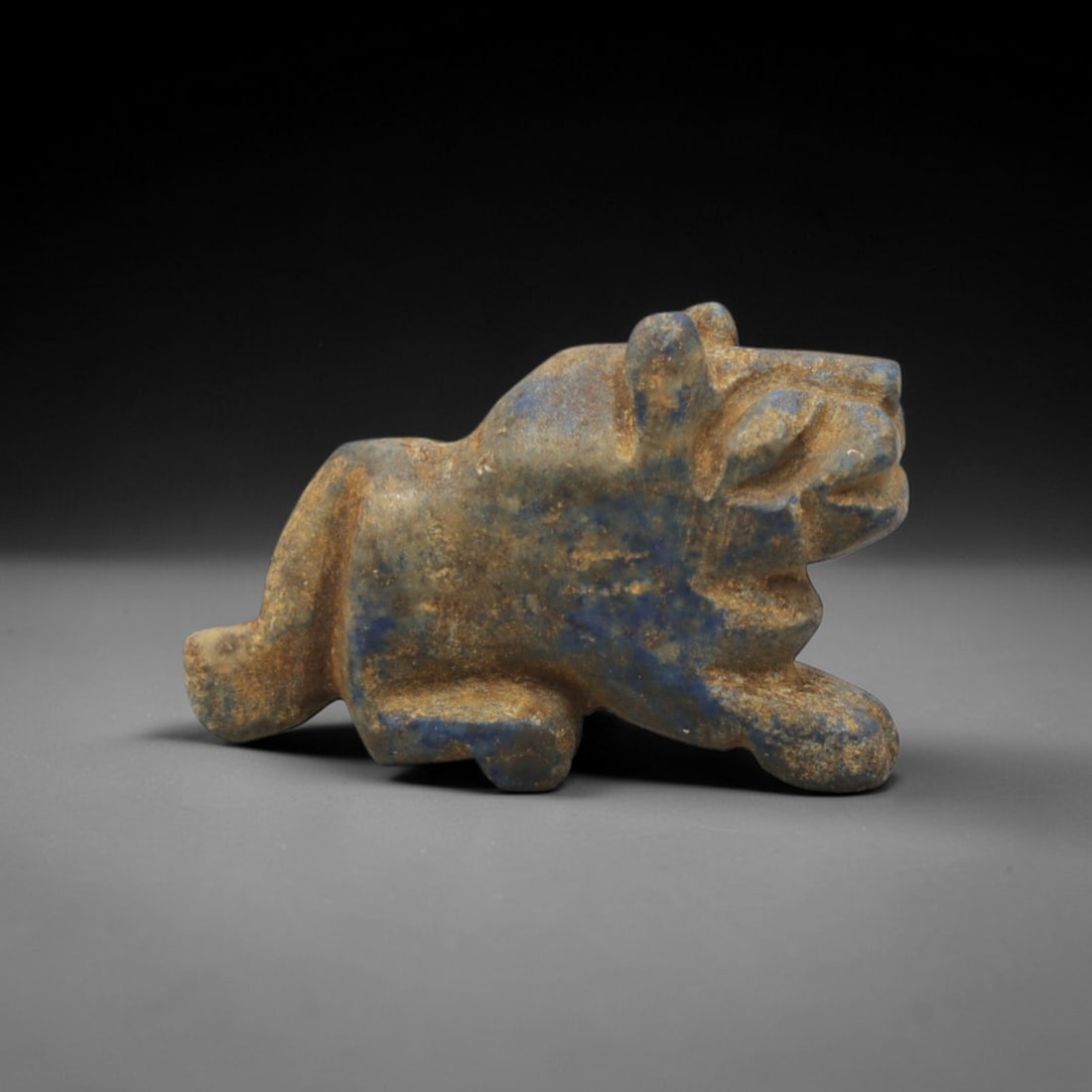 Ancient Lapis Lazuli Feline - Near Eastern Amulet Figurine, 4XT: Carved from lapis lazuli, this amulet depicts a crouched feline in a predatory stance with stylized, blocky features. The head is rounded with incised eye and mouth detailing, small upright ears, and