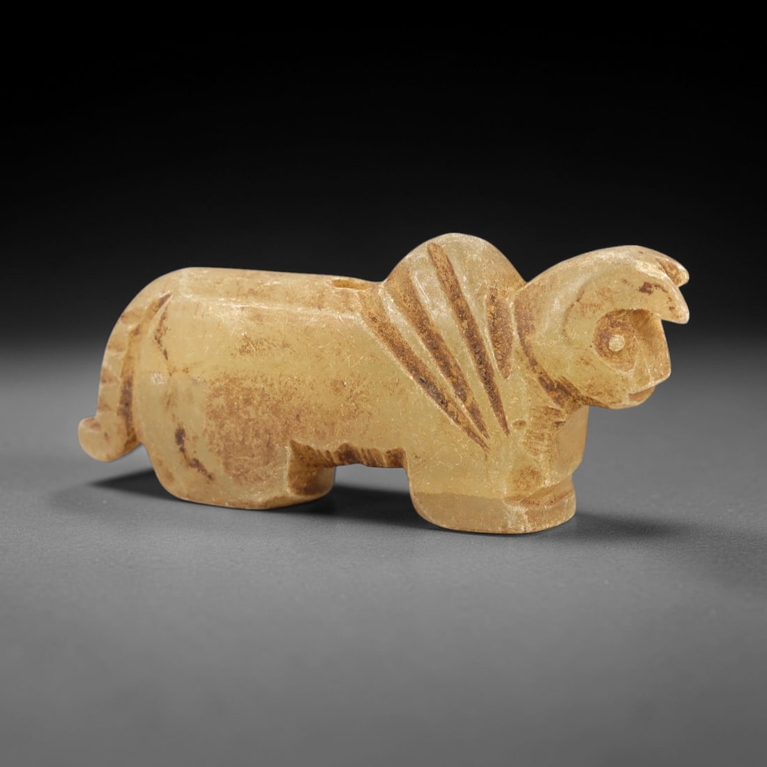 Ancient Rock Crystal Bovid Amulet - Near Eastern Figurine, 87AL: Carved from translucent pale yellow rock crystal, this amulet depicts a stylized recumbent bovid, likely a ram or sheep, with incised linear patterns along the neck and back to denote fur or mane. The