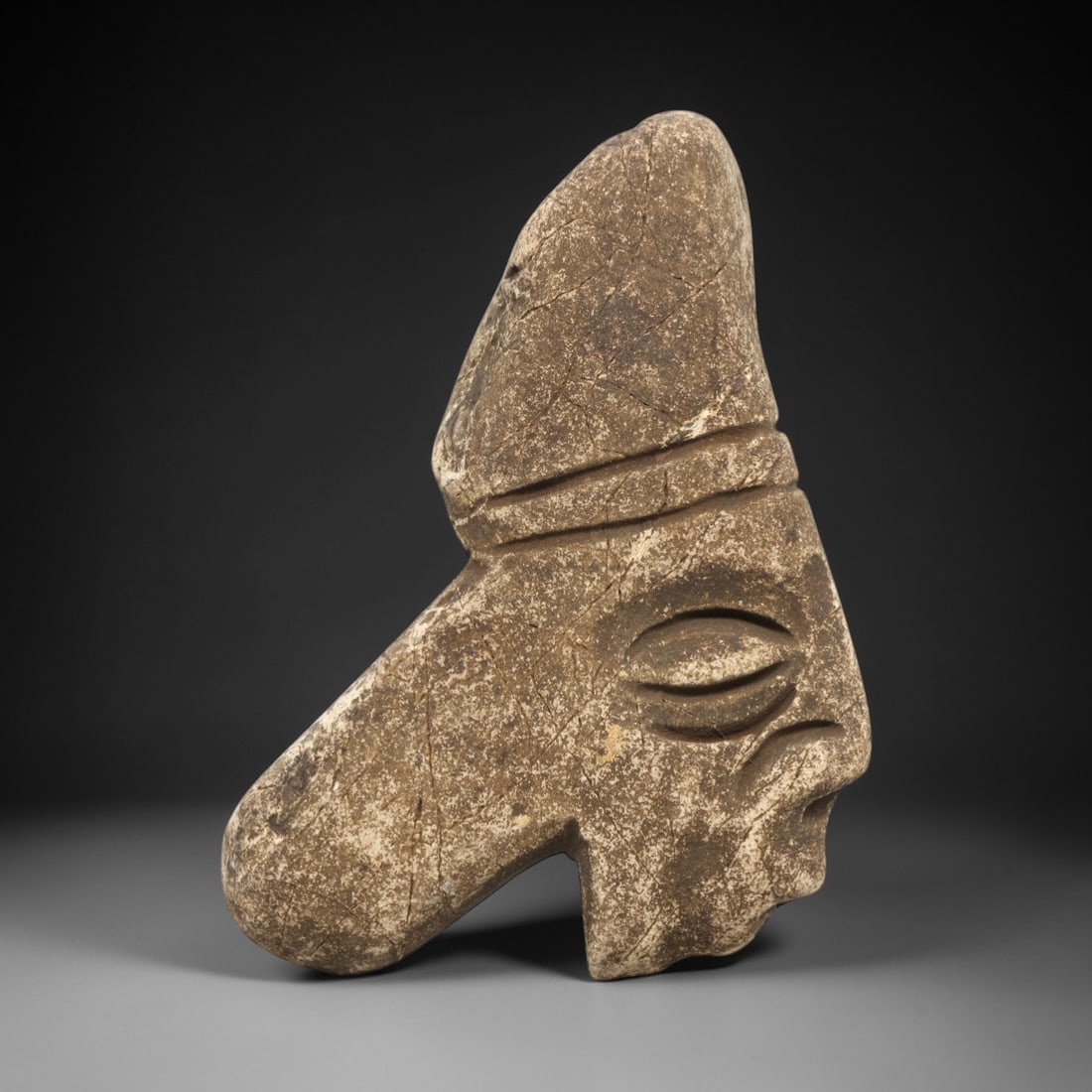 Ancient Stone Anthropomorphic Head - Near Eastern Idol, 91ZV: This artifact is a carved stone idol of anthropomorphic form, rendered in a granular, earth-toned stone consistent with ancient Near Eastern lithic traditions. The piece depicts a stylized male head s