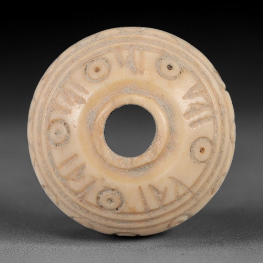 Ancient Bone Spindle Whorl - Near Eastern Dot-in-Circle Motif, 70XR: This ancient Near Eastern spindle whorl is crafted from bone, featuring incised dot-in-circle motifs encircling the central perforation. The compact, ring-like form is a traditional textile tool used