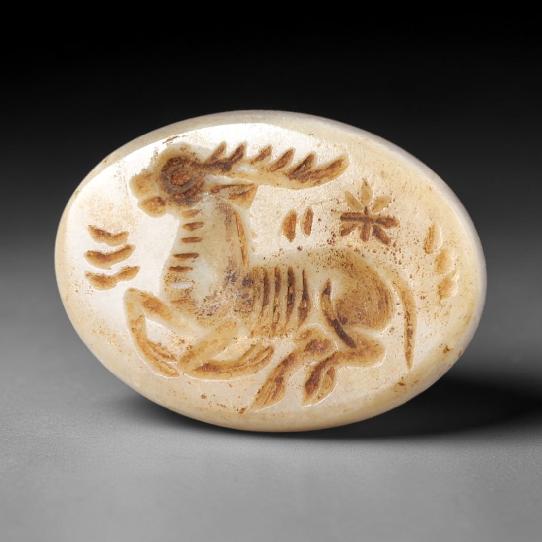 Ancient Stone Stag Intaglio - Near Eastern Amulet, 80AR: This oval intaglio is carved from a pale, creamy stone matrix, featuring a high-relief depiction of a stag in leaping pose, with branching antlers and incised linear details defining its ribcage, musc