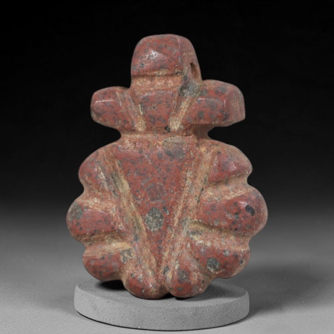 Ancient Stone Amulet - Near Eastern Ritual Figurine, 90AP: This artifact is carved from variegated red stone with a weathered, earthy patina and subtle mineral inclusions, exhibiting symmetrical, segmented detailing consistent with ancient Near Eastern stonew