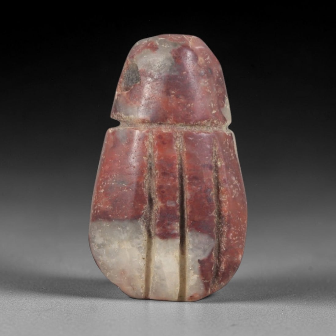 Ancient Stone Amulet - Egyptian Ritual Pendant, 55AP: This artifact is carved from variegated red and white stone with a weathered, earthy patina and natural mineral veining, exhibiting stylized vertical linear detailing consistent with ancient Egyptian