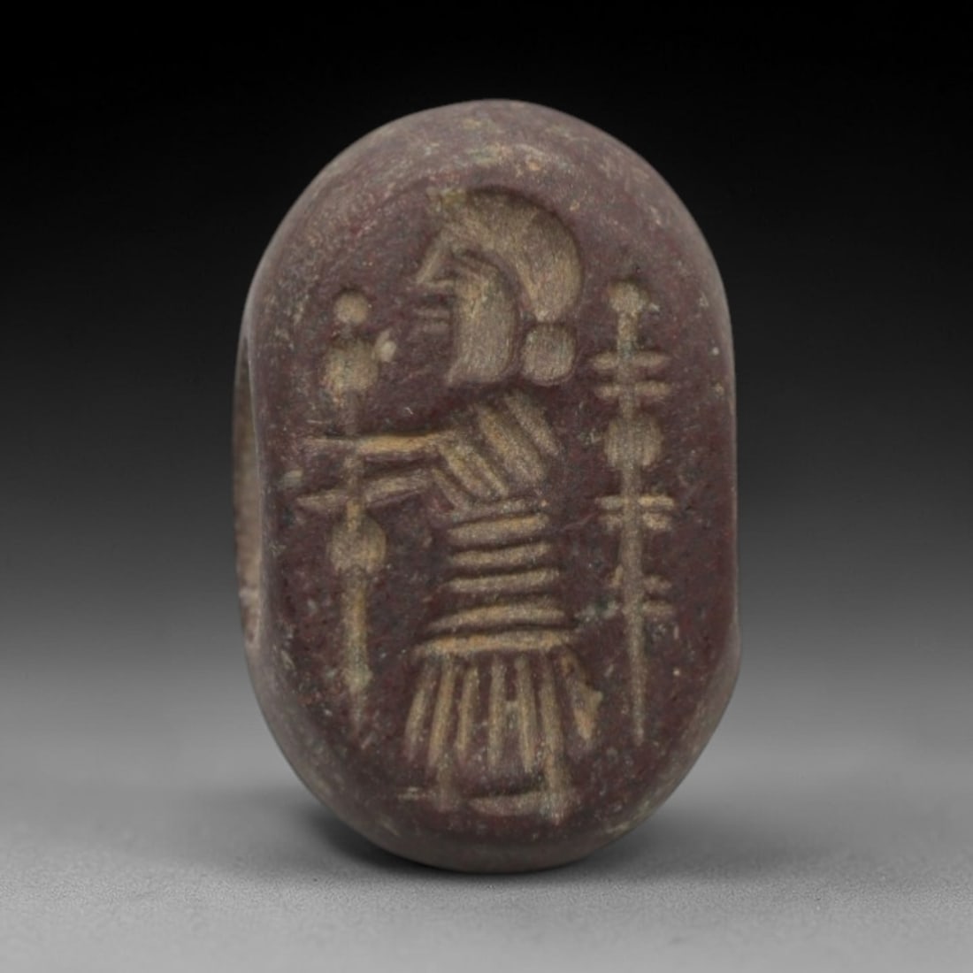 Ancient Stone Hemispherical Stamp Seal - Near Eastern Anthropomorphic Figure, 6ZT: Crafted from dense, reddish-brown stone, this hemispherical stamp seal bears finely incised carving of an anthropomorphic figure, depicted with a stylized headdress, segmented torso, and flared lower