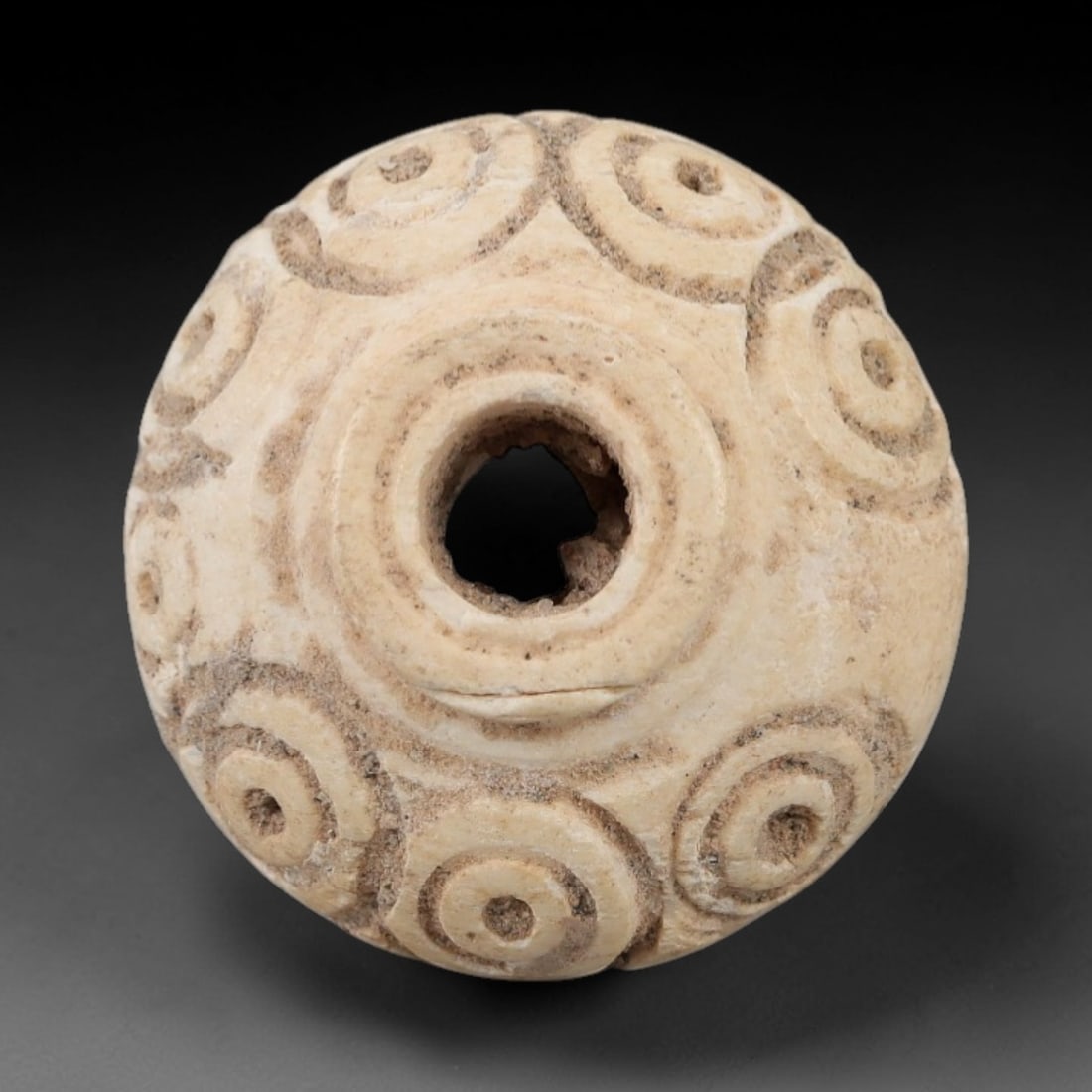 Ancient Bone Spindle Whorl - Near Eastern Concentric Circles, 4AJ: This ancient Near Eastern spindle whorl is carved from bone, exhibiting a biconvex form with a central perforation. The surface is decorated with incised concentric circular motifs, a common decorativ