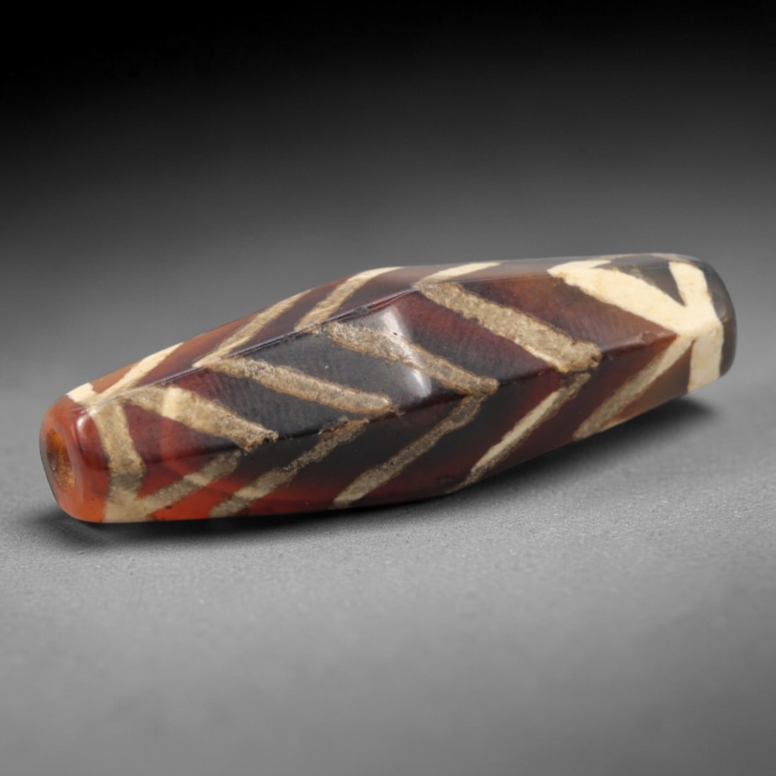Ancient Carnelian Chevron Dzi Bead - Himalayan Amulet, 83XV: Crafted from rich banded carnelian, this faceted bead features bold etched white chevron (V-shaped) linear patterns, executed in the traditional Himalayan Dzi bead technique. The form is an elongated,