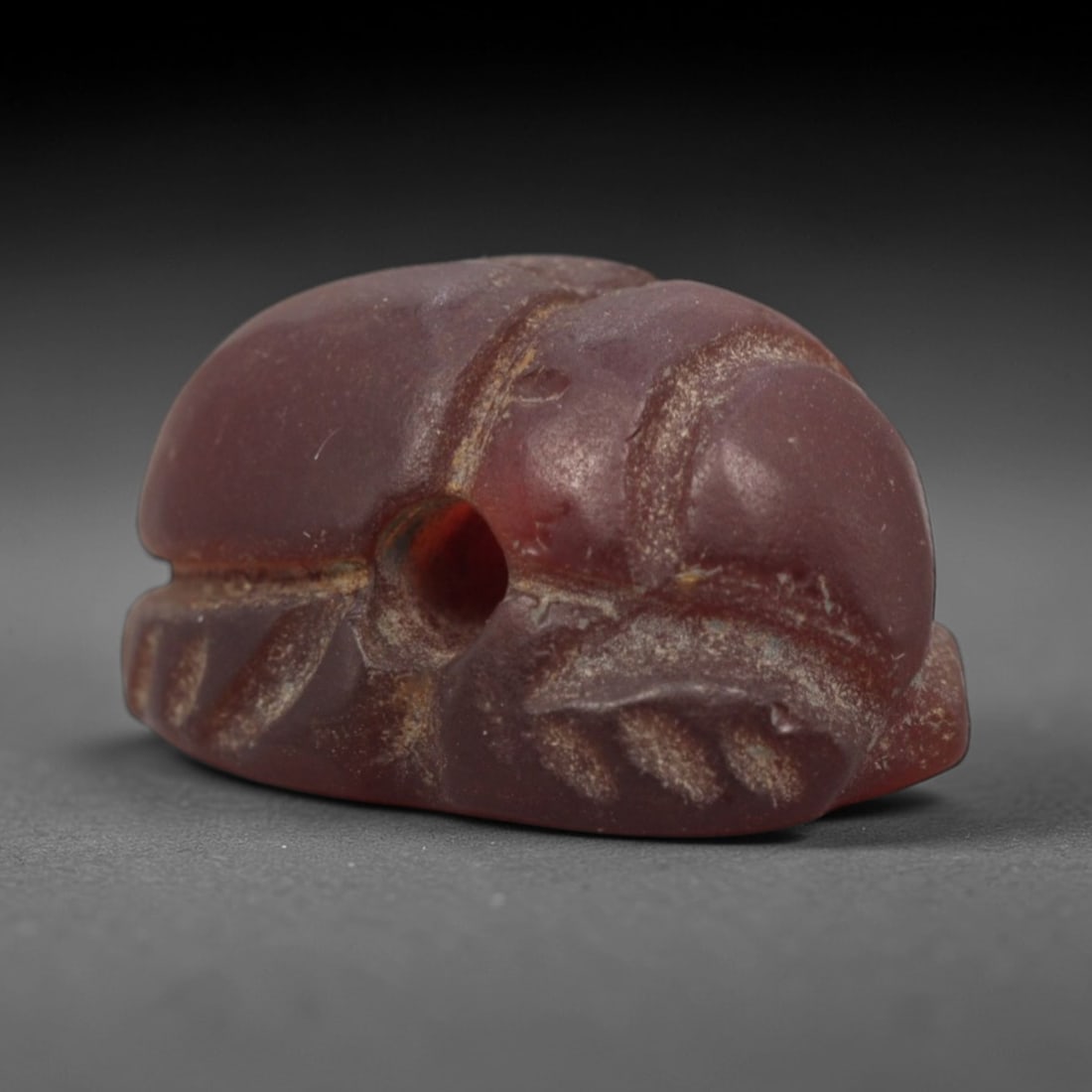 Ancient Carnelian Scarab Amulet - Egyptian Figurine, 58XS: Carved from rich, deep rose-red carnelian with subtle amber undertones and natural mineral patination, this amulet is formed as a stylized scarab beetle with incised linear detailing to define the cen